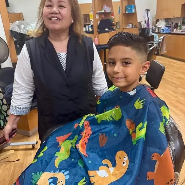 A smiling boy in a dinosaur cape after a fresh fade.